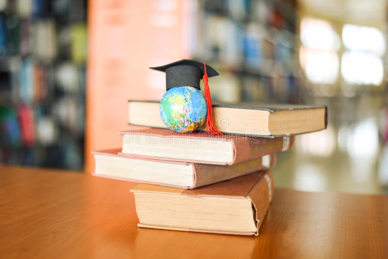 Books on the table in the library - Education learning old book stack and graduation cap on earth globe model on wood desk and