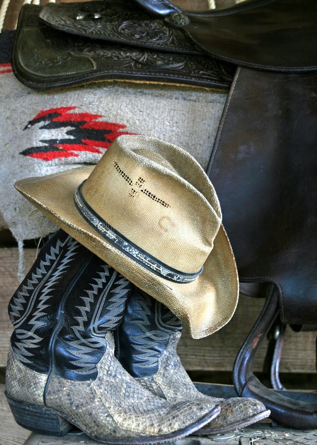 Cowboy hat on boots with saddle and blanket in back ground. Cowboy hat on boots with saddle and blanket in back ground