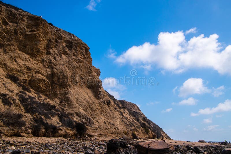 Bord brun déchiqueté rocailleux de falaise avec deux mouettes Fond profond de ciel bleu avec les nuages gonflés cassés photographie stock Bord brun déchiqueté rocailleux de falaise avec deux mouettes Fond profond de ciel bleu avec les nuages gonflés cassés photographie stock