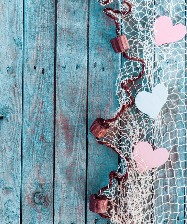 Border of romantic pink and white hearts in fishing net with an edge decoration of corks in vertical format on rustic turquoise blue boards with copyspace for your Valentine or anniversary greeting. Border of romantic pink and white hearts in fishing net with an edge decoration of corks in vertical format on rustic turquoise blue boards with copyspace for your Valentine or anniversary greeting