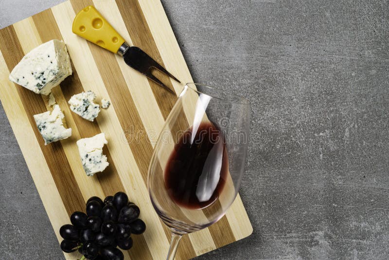 Bordo a strisce con formaggio e vetro con vino su fondo concreto Copi lo spazio immagine stock libera da diritti