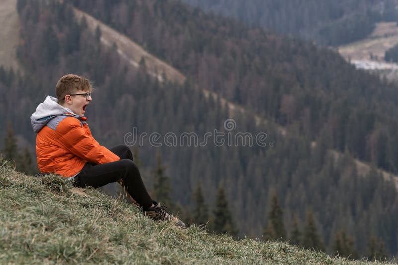 Bored guy sits on hillside and yawns. Boy screams in mountains. Portrait of child in the autumn on hike