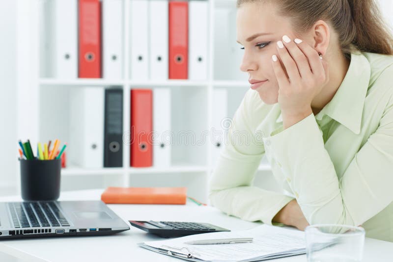 Bored young female office worker sits at her desk and looks at computer screen. royalty free stock photos Bored young female office worker sits at her desk and looks at computer screen. royalty free stock photos