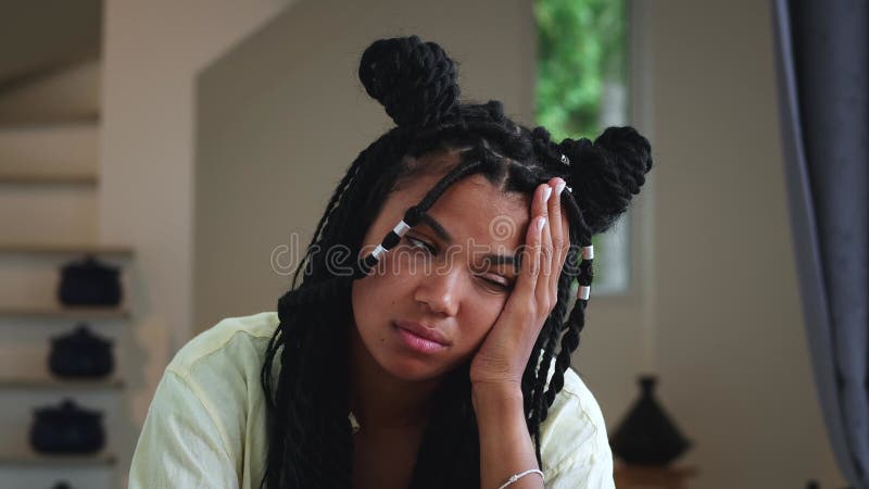 Close-up of a bored, exhausted young student woman feeling tired after work, sitting in living room and looking