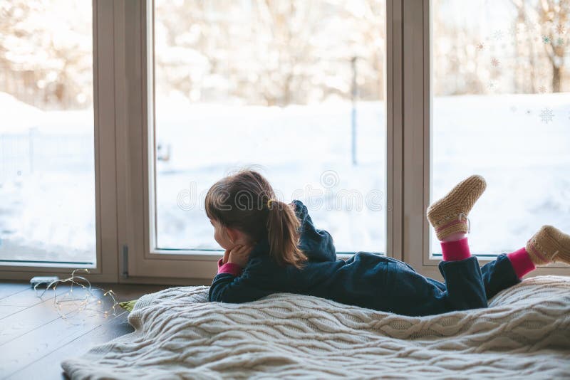 Boring little girl lying on a blanket near the window in winter