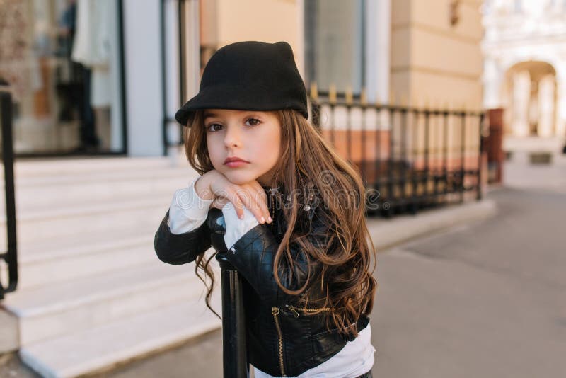 Boring lovely little girl in cute black hat waiting for mother outside in front of beauty saloon. Beautiful long-haired royalty free stock photo Boring lovely little girl in cute black hat waiting for mother outside in front of beauty saloon. Beautiful long-haired royalty free stock photo