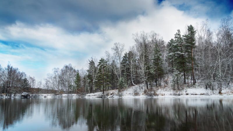 Bosque de invierno en el lago, nubes en el cielo y reflexión en el agua