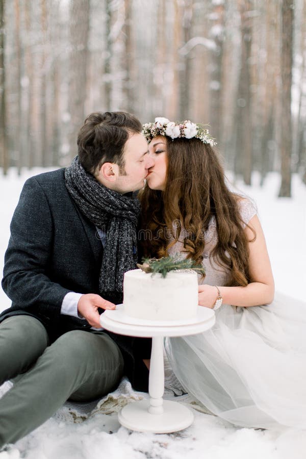 Bosque de invierno y historia de amor de boda Torta de invierno decorada, y hermosa pareja sentada y besada, bosque de invierno e imagen de archivo libre de regalías Bosque de invierno y historia de amor de boda Torta de invierno decorada, y hermosa pareja sentada y besada, bosque de invierno e imagen de archivo libre de regalías