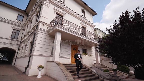 Bossy Man in Black Suit and Bow Tie Goes Down Marble Stairs Out