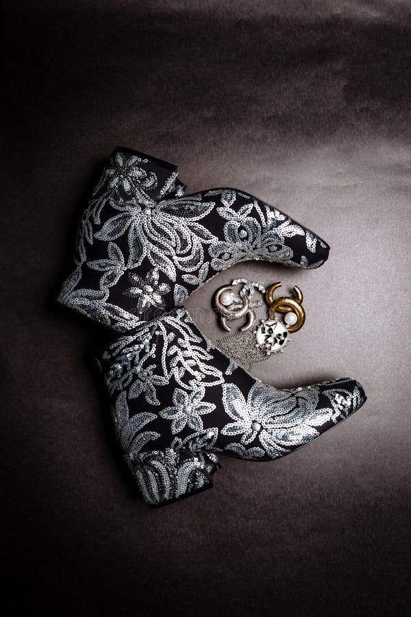 Botas grosso-colocadas saltos pretas do tornozelo decoradas com as flores bordadas com lantejoulas e os broches de prata em um fu foto de stock Botas grosso-colocadas saltos pretas do tornozelo decoradas com as flores bordadas com lantejoulas e os broches de prata em um fu foto de stock