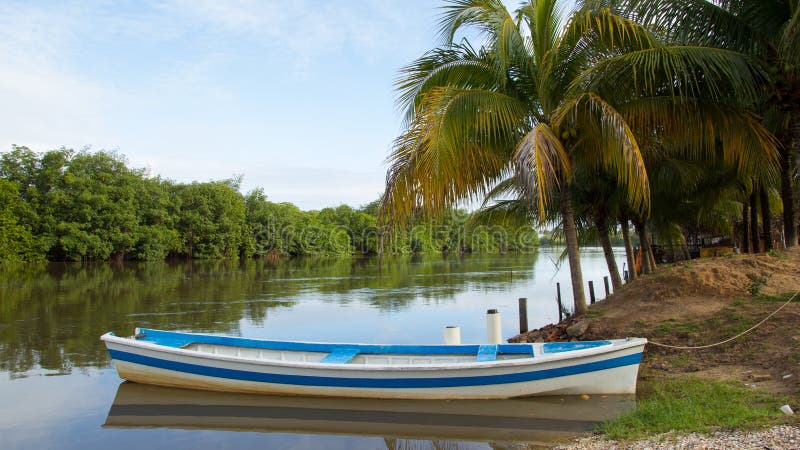 Bote pequeño en el borde del ` s del río Pintura azul y blanca foto de archivo libre de regalías Bote pequeño en el borde del ` s del río Pintura azul y blanca foto de archivo libre de regalías