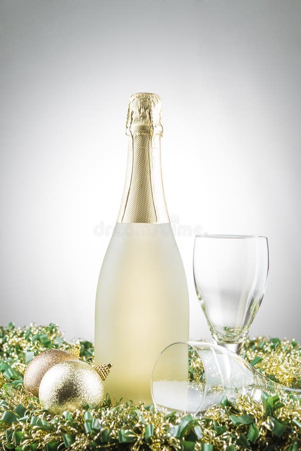 Botella de champán, de decoraciones de la Navidad y de dos vidrios en las guirnaldas con el fondo blanco de la pendiente foto de archivo Botella de champán, de decoraciones de la Navidad y de dos vidrios en las guirnaldas con el fondo blanco de la pendiente foto de archivo