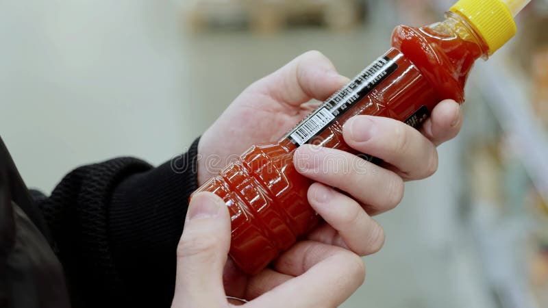 Botella de salsa en las manos. cliente con una chaqueta negra examina y pone una botella de salsa picante en un supermercado metrajes