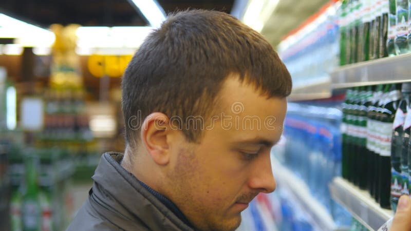 Botella que elige y de compra del hombre joven de agua mineral en el supermercado Individuo que toma el producto de estantes en e