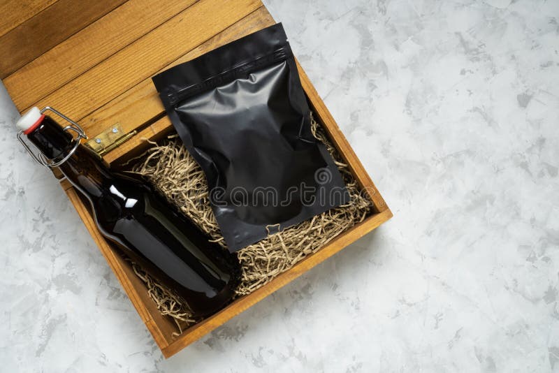 Bottiglia di birra artigianale e imballaggio di spuntini in una scatola regalo di legno su fondo di calcestruzzo grigio con spazio immagini stock