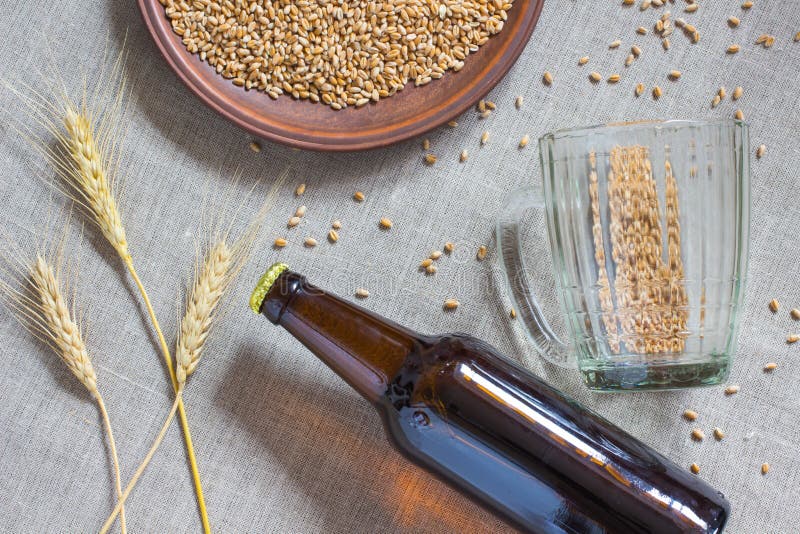 Bottiglia di birra, grano, tazza vuota su tela di sacco immagini stock Bottiglia di birra, grano, tazza vuota su tela di sacco immagini stock