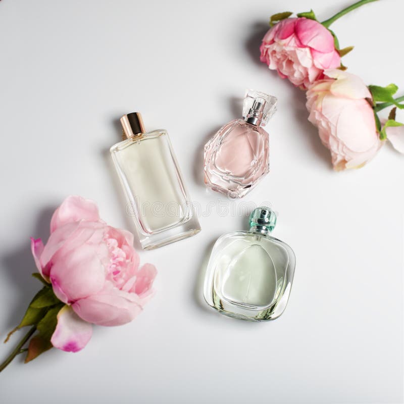 Bottiglie di profumo con i fiori su fondo leggero Profumeria, cosmetici, raccolta di fragranza Disposizione piana