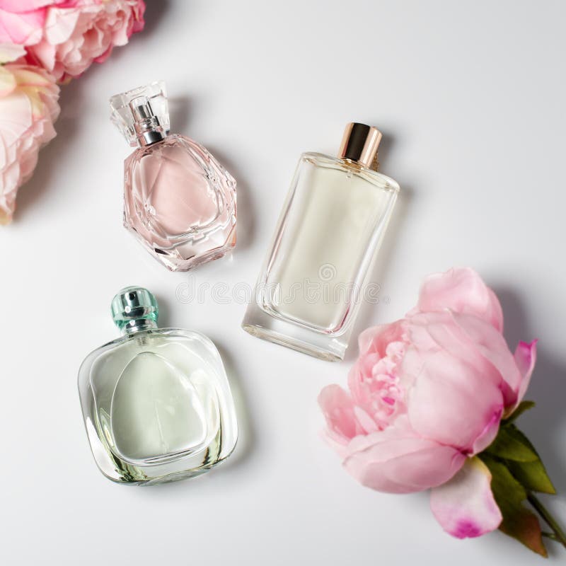 Bottiglie di profumo con i fiori su fondo leggero Profumeria, cosmetici, raccolta di fragranza Disposizione piana