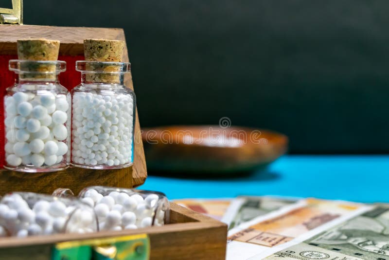 Bottiglie di vetro della medicina omeopatica delle pillole in scatola di legno su valuta indiana e nella superficie blu con il cu immagini stock Bottiglie di vetro della medicina omeopatica delle pillole in scatola di legno su valuta indiana e nella superficie blu con il cu immagini stock