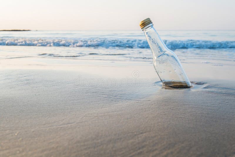 Empty Glass Bottle On Sandy Beach With Blue Sky And Sea Stock Photo
