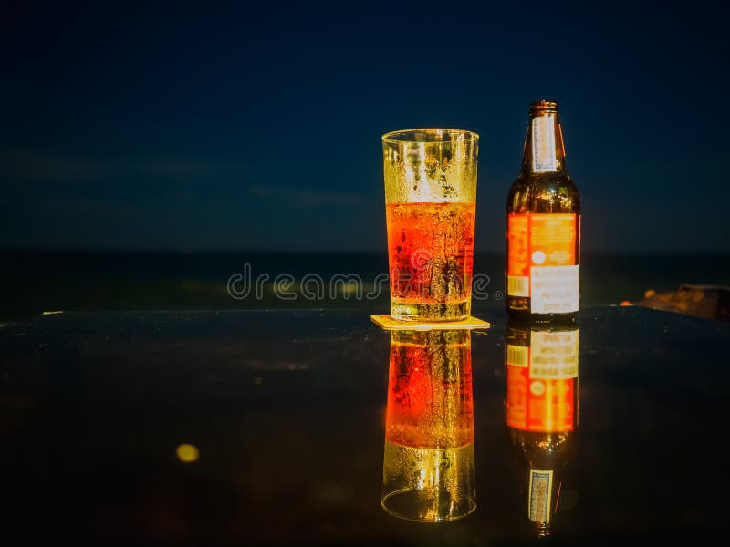 Bottle and Glass of Beer on the Table at the Beach during Night Stock
