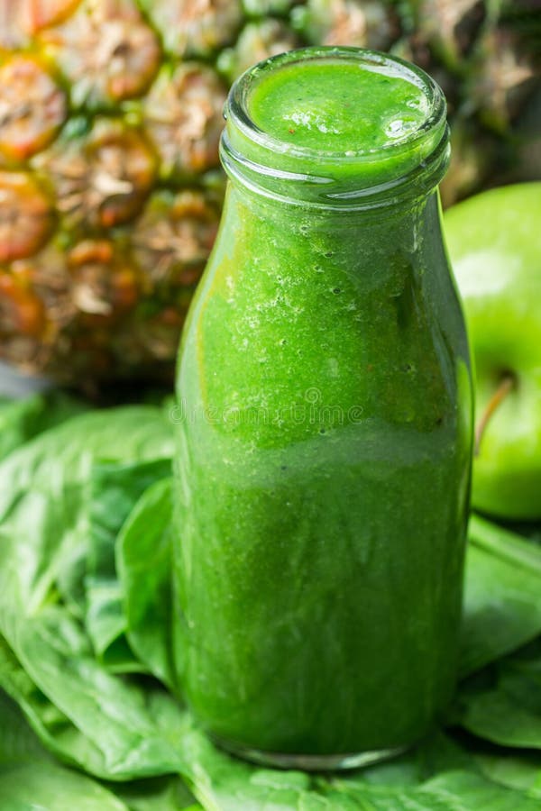 Bottle with Green Fresh Raw Smoothie from Leafy Greens Vegetables Fruits Apples Pineapple Bananas Kiwi Zucchini on Spinach leaves