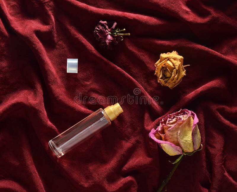 A bottle of perfume and buds of dried roses on a red silk background. Romantic look. Top view