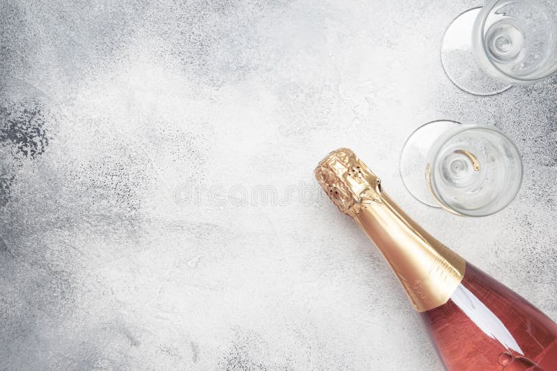 Bottle with pink sparkling wine or rose champagne and glasses, gray background with place for text, holiday or date concept, flat lay, top view