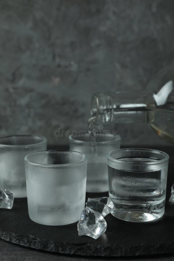 A Bottle with Pouring Vodka and Shots of Vodka on Black Tray Stock
