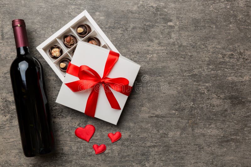 Bottle of red wine on colored background for Valentine Day with gift and chocolate. Heart shaped with gift box of