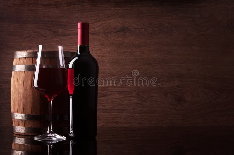 Bottle of red wine, glass and barrel on wooden background