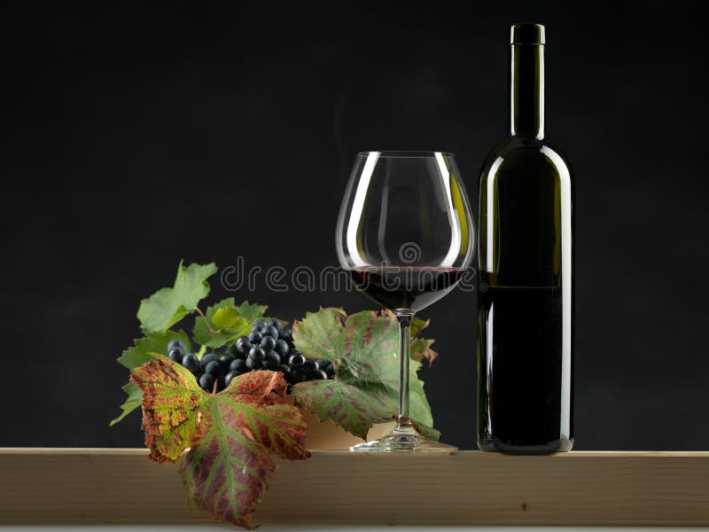 Bottle red wine, glass, grapes black background