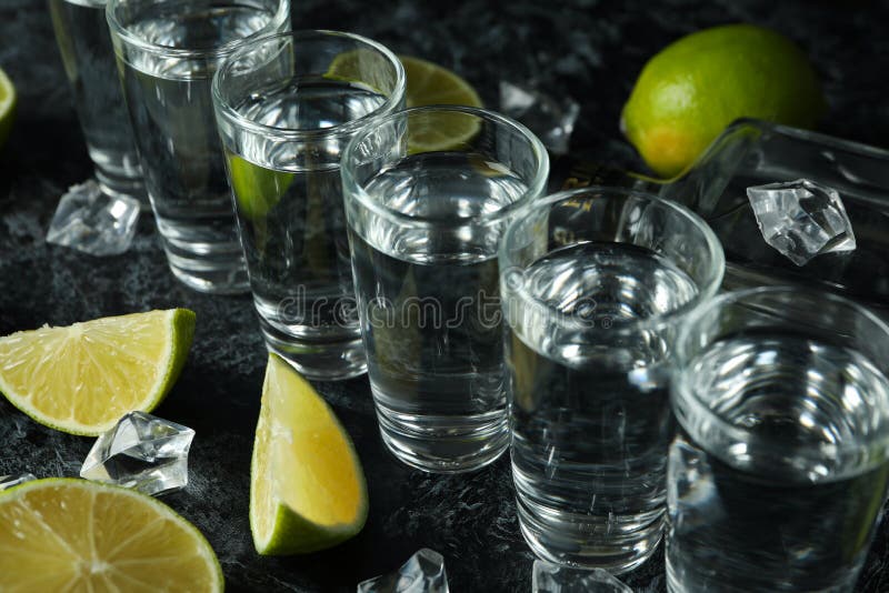 Bottle of Vodka, Shots, Ice Cubes and Lime Slices on Black Smokey Table