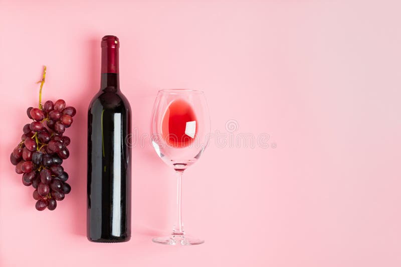 A bottle of wine an empty glass of a bunch of grapes on a gentle pink background. Minimalism. Top view flat layout royalty free stock images A bottle of wine an empty glass of a bunch of grapes on a gentle pink background. Minimalism. Top view flat layout royalty free stock images