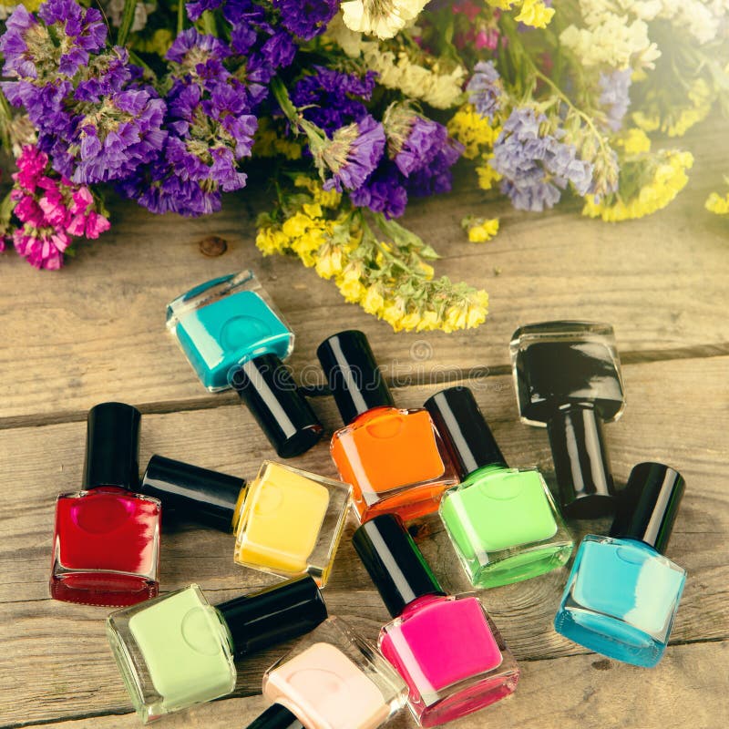 Bottles Of Colorful Nail Polish And Flowers On Wooden Table