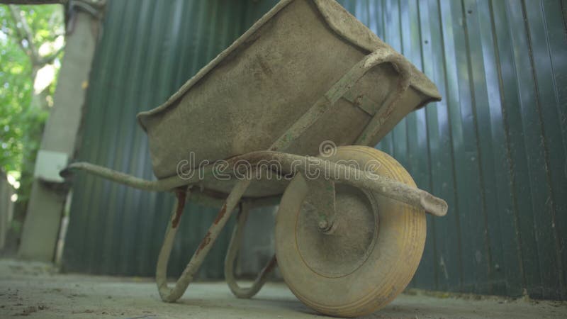 Bottom view of rusty dirty industrial cart standing on neglected factory or plant. Side view of abandoned wheelbarrow on