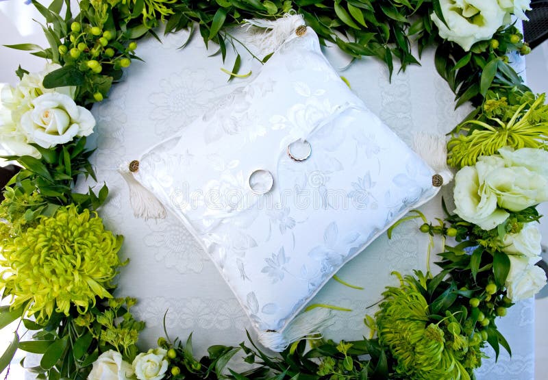 Boucles de mariage sur un coussin blanc dans une guirlande des fleurs photo libre de droits Boucles de mariage sur un coussin blanc dans une guirlande des fleurs photo libre de droits
