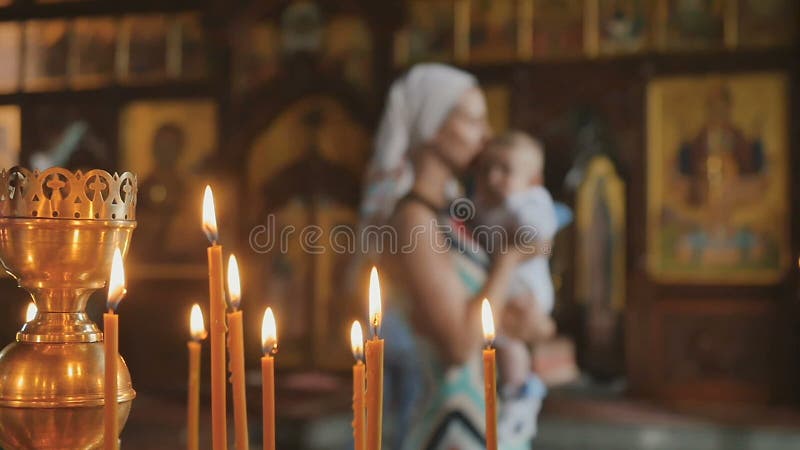 Bougies brûlantes dans l'église, mère avec le bébé sur le fond brouillé