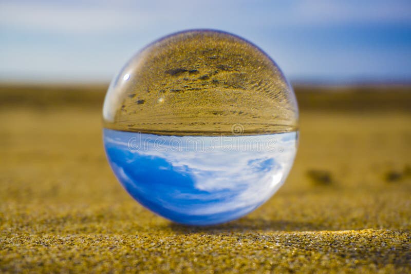 Boule en verre se situant en sable dans la perspective des vagues de mer et ciel avec des nuages images libres de droits Boule en verre se situant en sable dans la perspective des vagues de mer et ciel avec des nuages images libres de droits