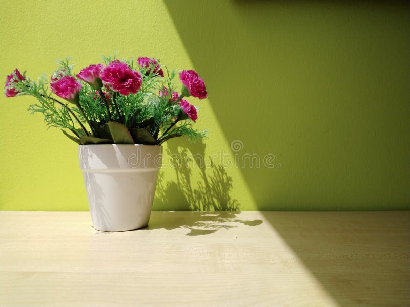 A bouquet of flowers in a vase on a wooden table and a green backdrop by the window and sunlight.