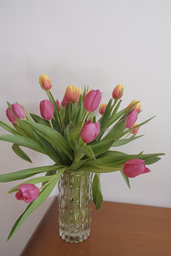 bouquet of pink and yellow tulips in vase closeup across white all on the wooden drawer. Interior detail. Hotel interior.