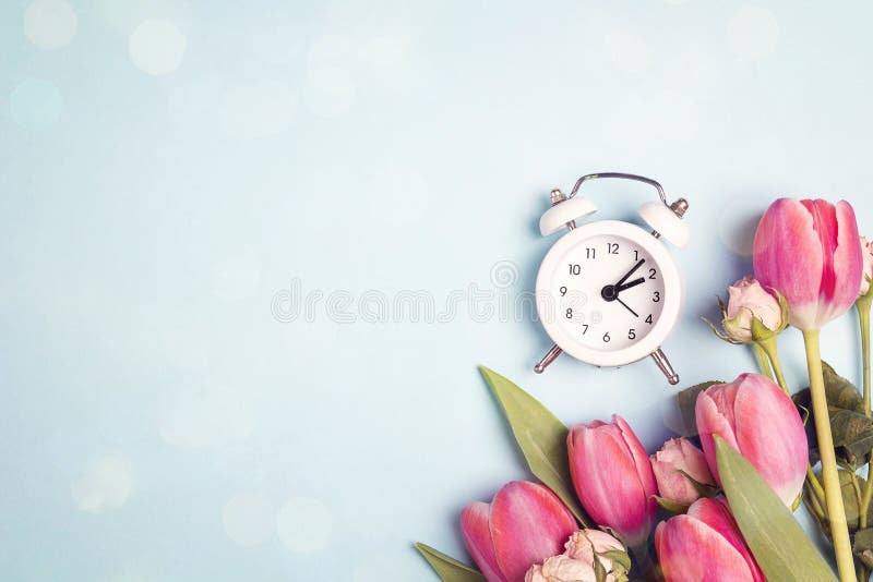 A bouquet of tulips and small roses with a white alarm clock on a blue background. Place for text