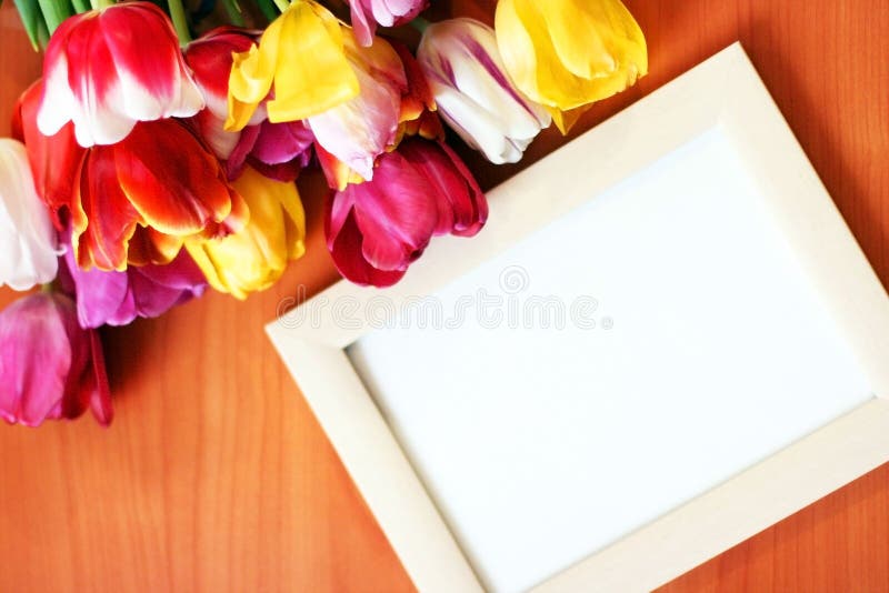 Bouquet of tulips and white mockup frame on wooden background. Easter or Birth Day greeting mock up. royalty free stock photography Bouquet of tulips and white mockup frame on wooden background. Easter or Birth Day greeting mock up. royalty free stock photography