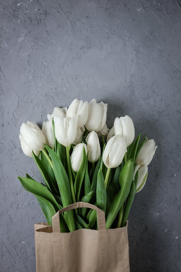 Bouquet of white tulips in a kraft paper bag on a gray concrete background. Top view. Flat lay. Postcard for Easter