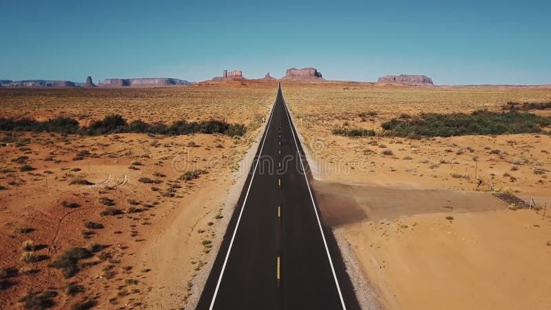 Bourdon volant vers l'arrière au-dessus de la route vide iconique de désert de grès en vallée de monuments, Arizona avec de grand