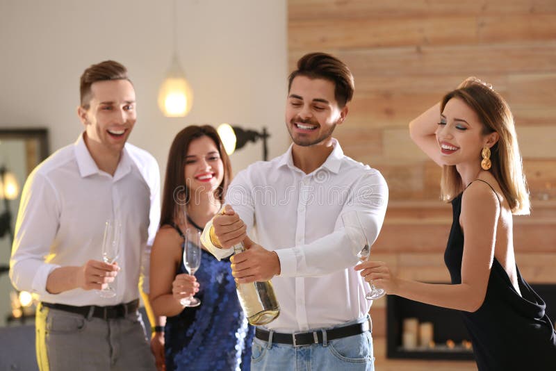 Bouteille d'ouverture d'homme de champagne parmi des amis photo libre de droits Bouteille d'ouverture d'homme de champagne parmi des amis photo libre de droits
