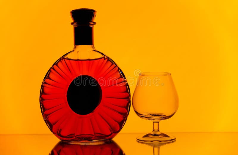 Bouteille de cognac et verre de verre ballon sur le fond jaune d'or images stock Bouteille de cognac et verre de verre ballon sur le fond jaune d'or images stock