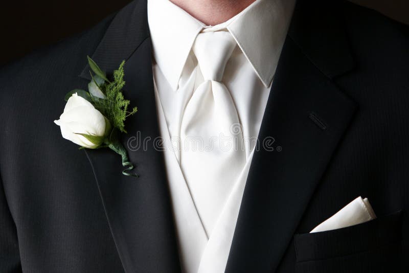 Wedding boutonniere pinned on the collar of a black wedding suit with white tie and handkerchief in pocket. Wedding boutonniere pinned on the collar of a black wedding suit with white tie and handkerchief in pocket