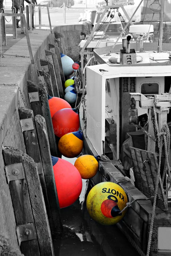 Black and white photo of fishing boats moored in whitstable harbour with colour popped buoys. Black and white photo of fishing boats moored in whitstable harbour with colour popped buoys.