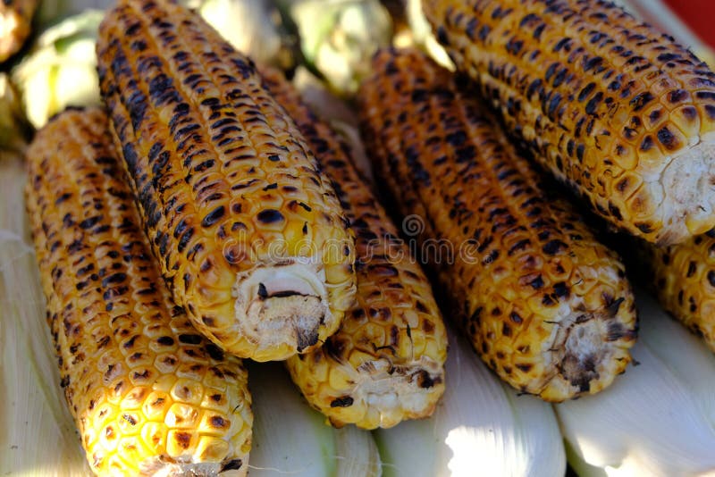 Bovenaanzicht keukentafel met gegrilde suikermaïskolf onder smeltboter en groenen op bakpapier stock afbeeldingen Bovenaanzicht keukentafel met gegrilde suikermaïskolf onder smeltboter en groenen op bakpapier stock afbeeldingen